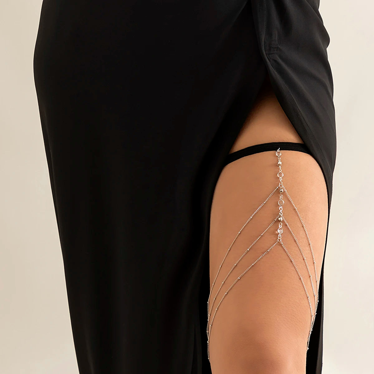 A close-up of a woman wearing a black dress, showcasing boho crystal leg thigh body chain jewelry on her skin.