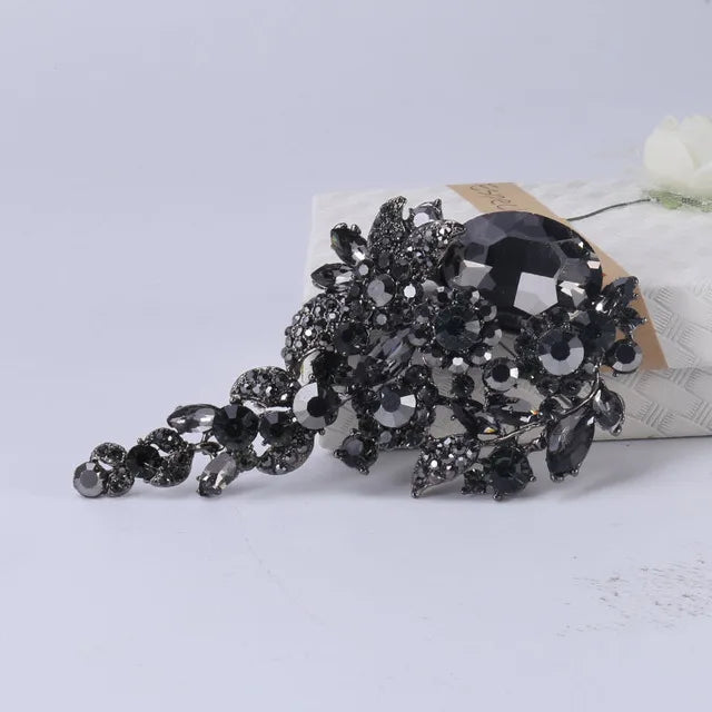 Un cluster de fleurs et de pierres de cristal noir formant une épingle élégante sur fond blanc.