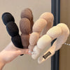 A hand holds several cloud sponge hair accessories headbands in shades of black, brown, and beige.