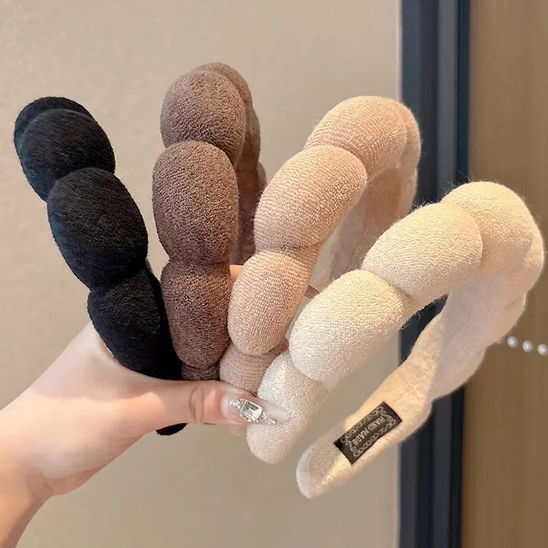 A hand holds several cloud sponge hair accessories headbands in shades of black, brown, and beige.