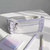 A white lace pencil case is shown open on a white surface next to a notebook and a pencil.