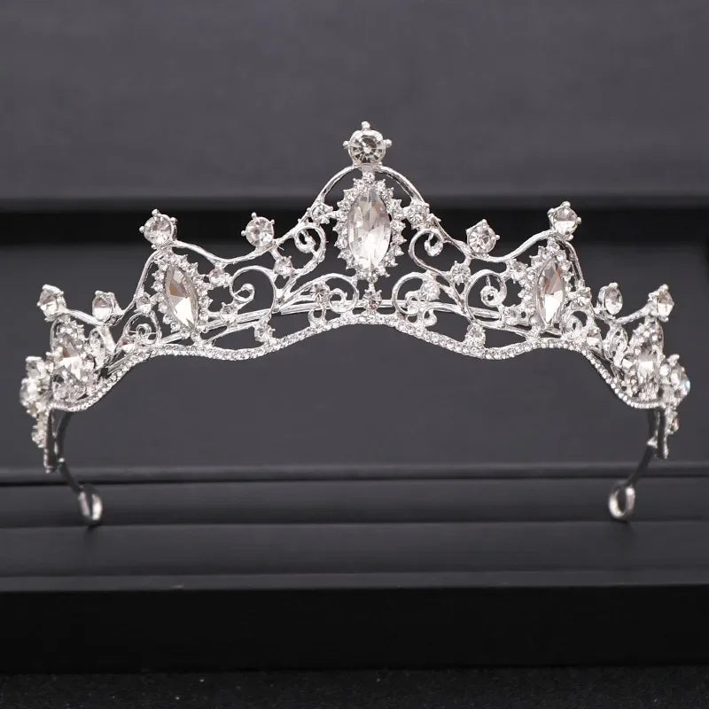 A sparkling crystal bridal crown with intricate silverwork and diamond-like stones displayed on a dark background.