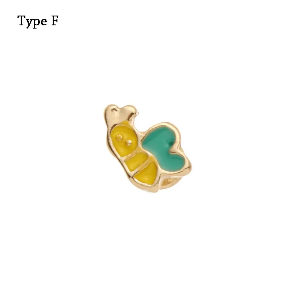 Adorno de pulsera de metal decorativo con forma de abeja amarilla y detalle de corazón turquesa.