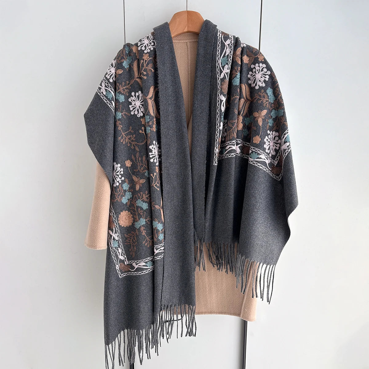 A gray luxury floral scarf with white snowflake embroidery and fringe, displayed on a wooden hanger.