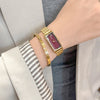A close-up of a vintage gold stainless steel quartz watch worn on a wrist, paired with a striped cuff.