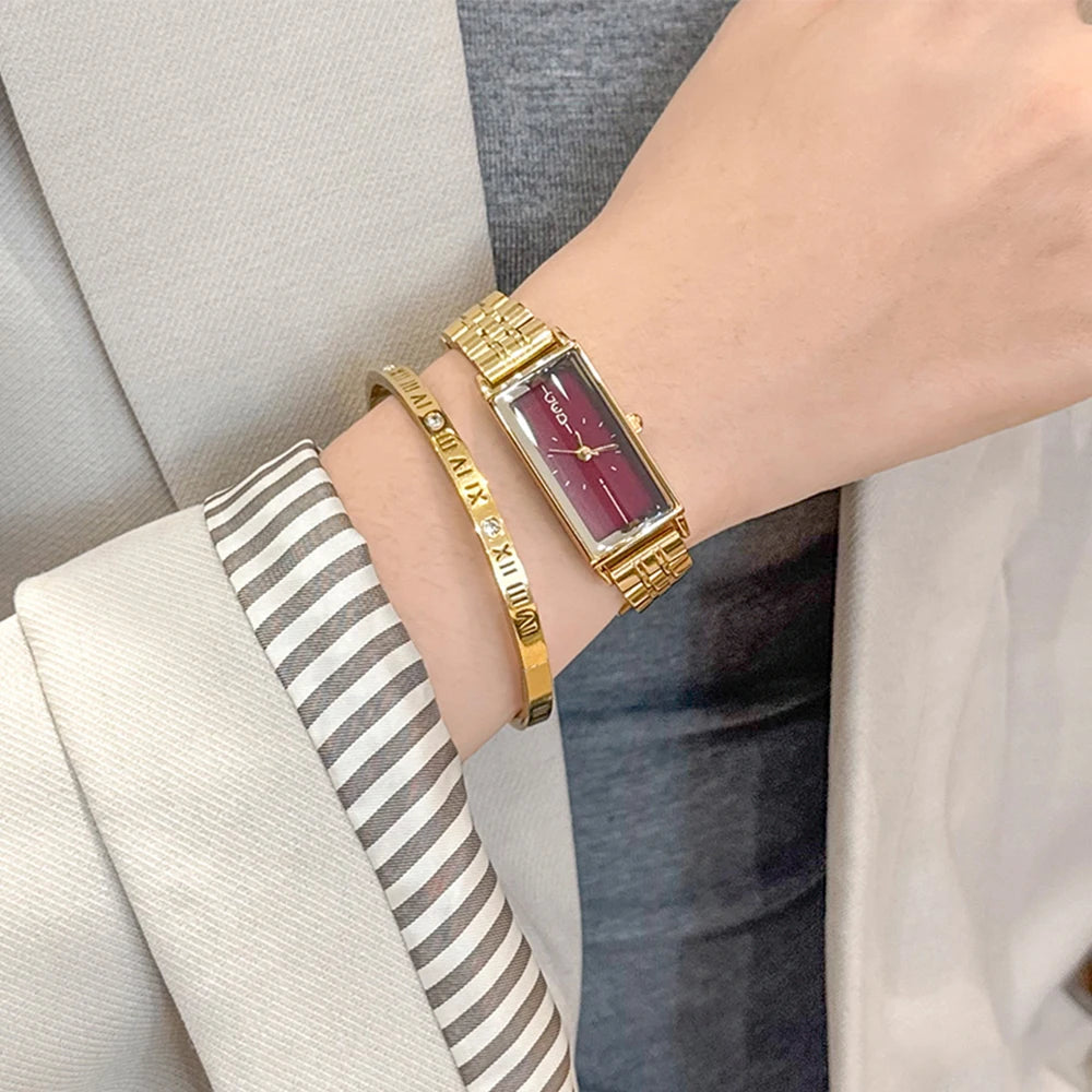 A close-up of a vintage gold stainless steel quartz watch worn on a wrist, paired with a striped cuff.