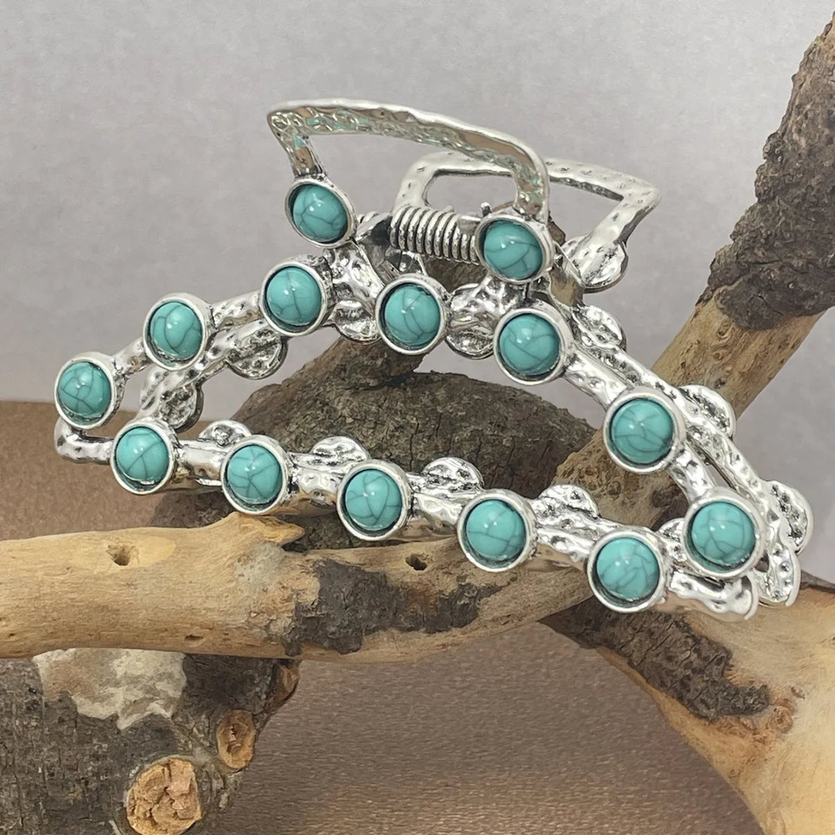 Silver metal hair claw clips decorated with turquoise beads resting on a piece of wood.