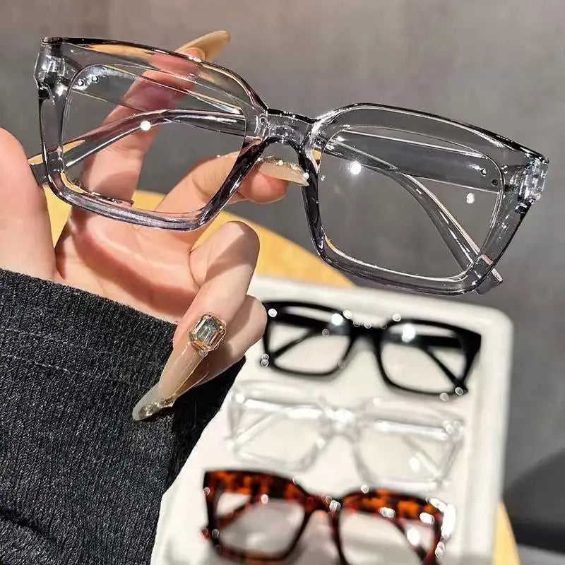 A hand holds a pair of clear, square-framed reading glasses against a dark sleeve.