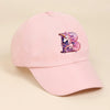 A pink baseball cap featuring a purple and iridescent unicorn letter design.