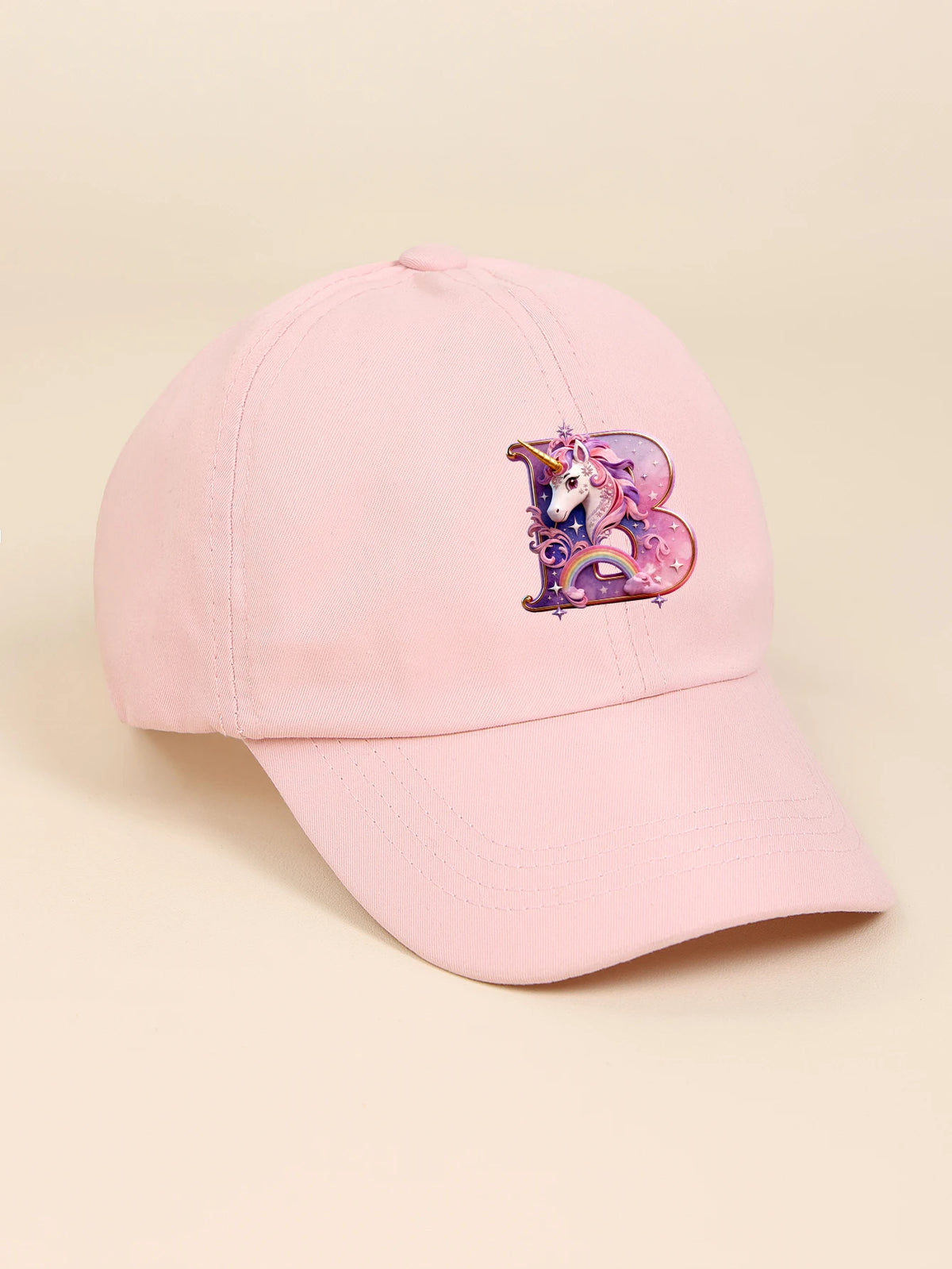 A pink baseball cap featuring a purple and iridescent unicorn letter design.