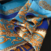 A close-up of a blue silk scarf featuring intricate gold and orange baroque patterns.