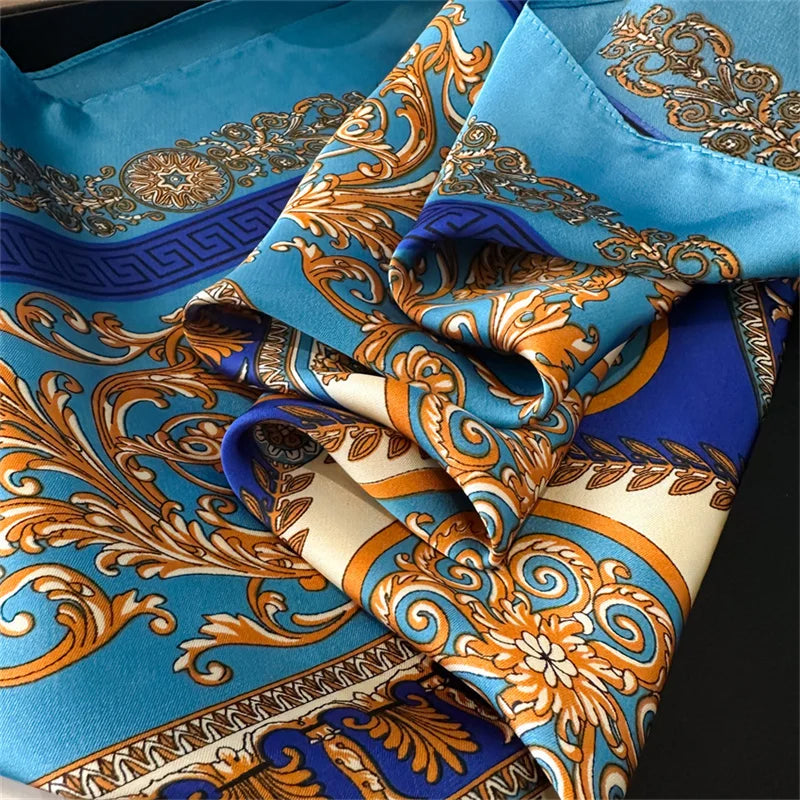 A close-up of a blue silk scarf featuring intricate gold and orange baroque patterns.