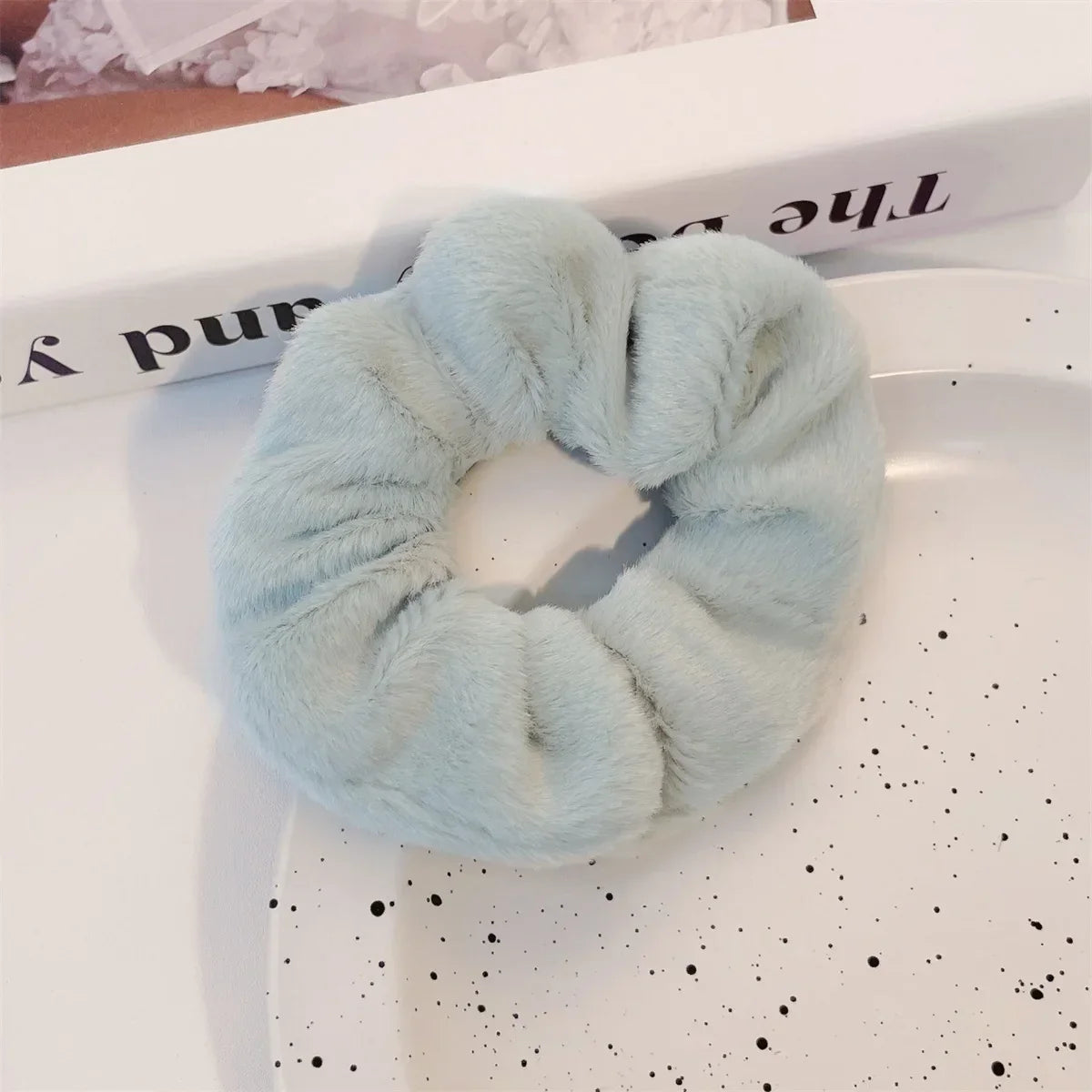 Un élastique pour cheveux en tricot flou bleu clair est exposé sur une assiette blanche à côté d'un livre.