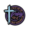 A black enamel lapel pin featuring a light blue cross and the text Pray on it Pray over it Pray through it in purple script.