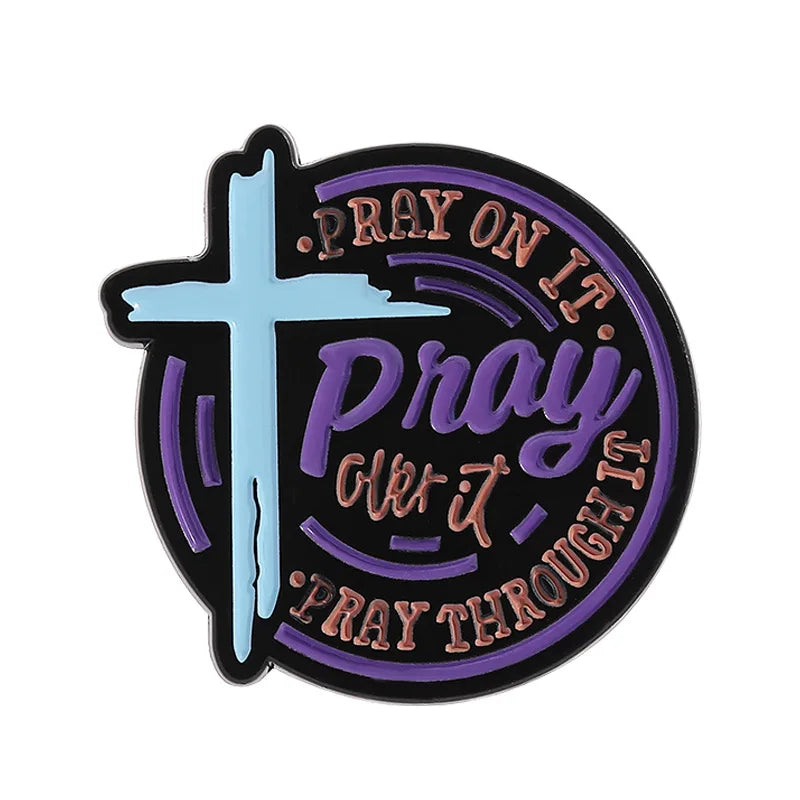 A black enamel lapel pin featuring a light blue cross and the text Pray on it Pray over it Pray through it in purple script.