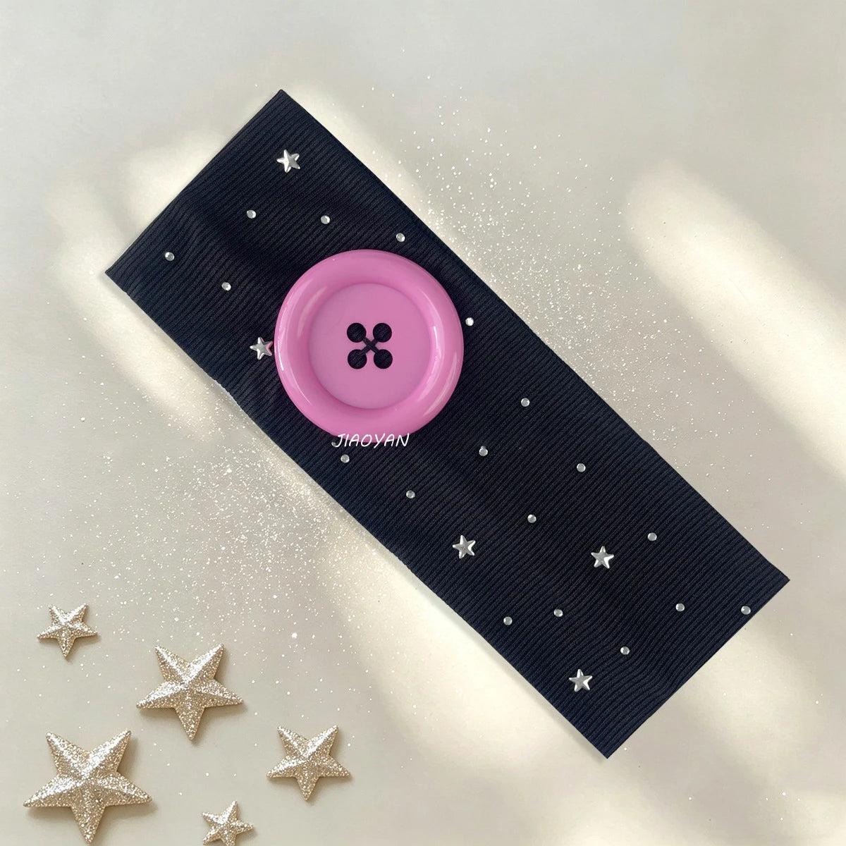 A dark blue polka dot headband with a pink button and silver stars scattered on a light background.