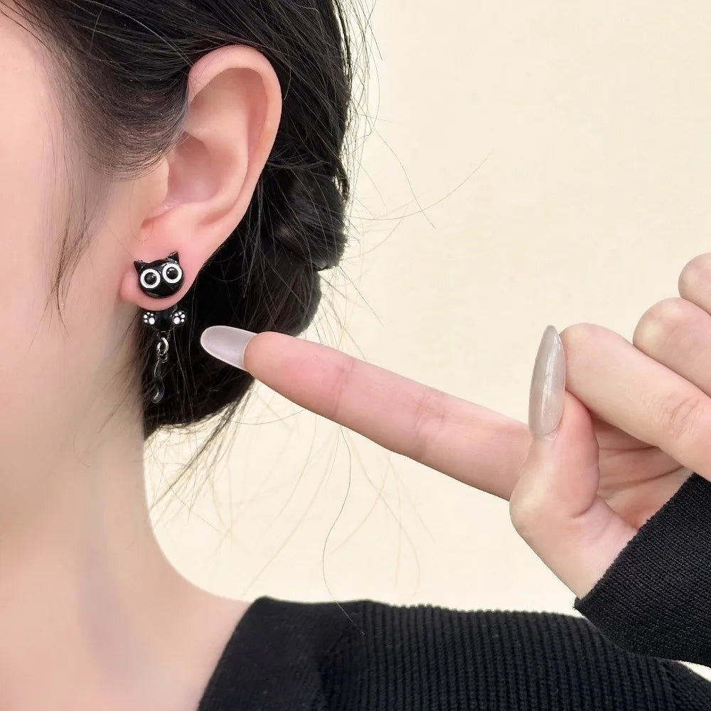 A close-up of a woman's ear showing cute black cat stud earrings and a hand holding them.