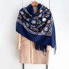 A navy blue luxury floral scarf with embroidered white and beige floral patterns draped over a beige coat.