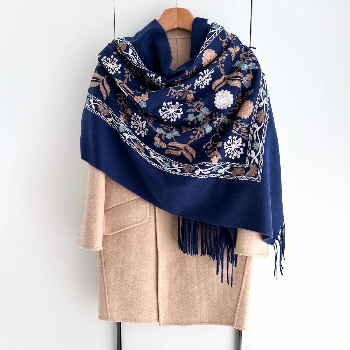 A navy blue luxury floral scarf with embroidered white and beige floral patterns draped over a beige coat.