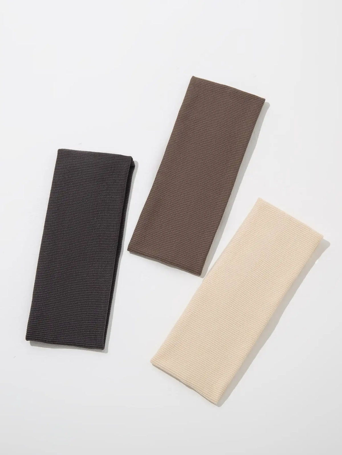 Three solid color fashion headbands in black, brown, and beige laid diagonally on a white background.