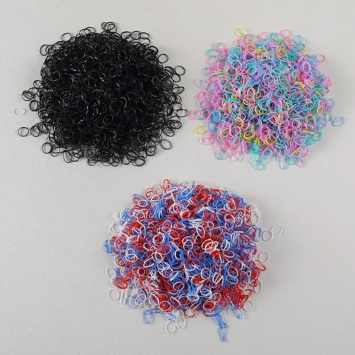 Three piles of colorful disposable rubber hair ties in black, pink, and red.