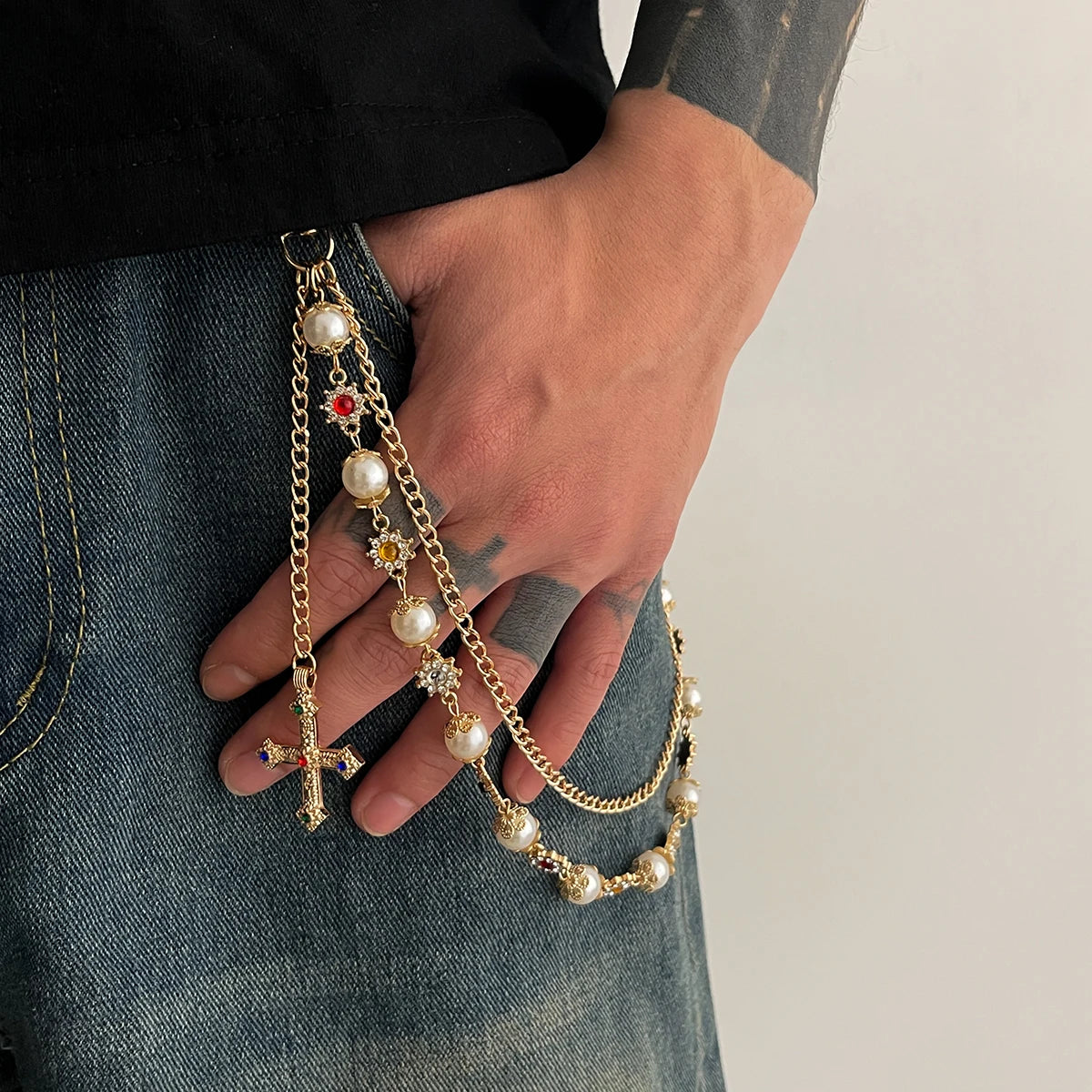 A hand is holding a gold chain with pearl beads and a cross pendant against a denim background.