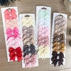 Un set de pinzas para el pelo con forma de lazo de colores sólidos para niños, incluyendo rosa, rojo, morado y beige.
