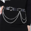 Un vestido negro con un cinturón de cadena de corazón plateada y correas de cuero con herrajes plateados.