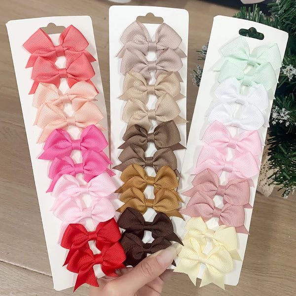 A collection of solid color kids bow hair clips in various shades of pink, beige, and brown displayed on a white card.