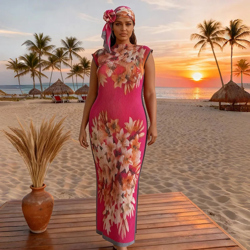 A plus size model wearing a pink and floral printed maxi dress and head wrap on a beach at sunset.