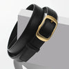 A black leather belt with a gold-toned buckle is displayed on a white surface.