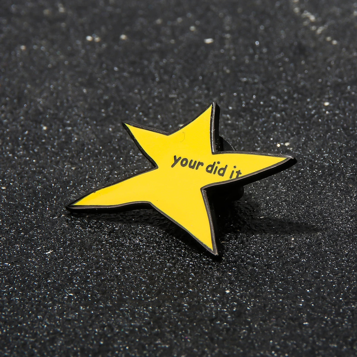 A yellow star shaped enamel pin with the text your did it on a black surface.