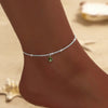 A delicate silver sparkling zircon heart cross anklet worn on a person's ankle against a light background.