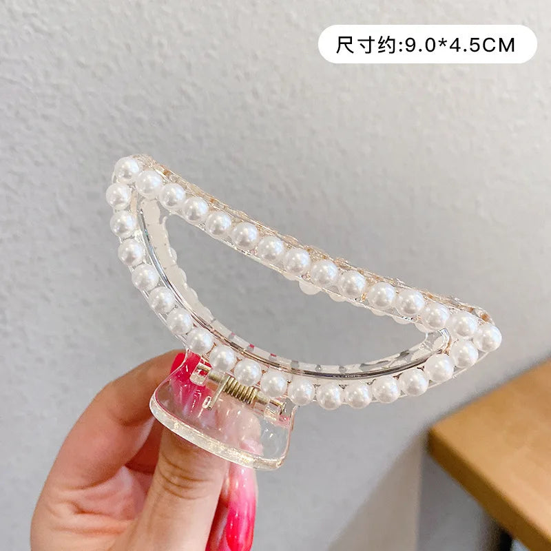 A clear plastic hair claw with a pearl design is being held by a hand against a white background.