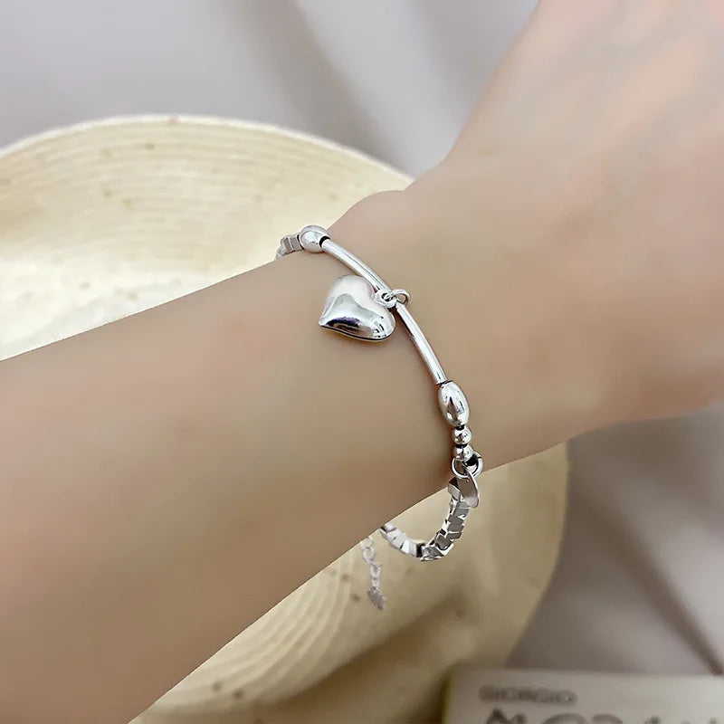 A close-up of a sterling silver double heart charm bracelet worn on a wrist against a light background.