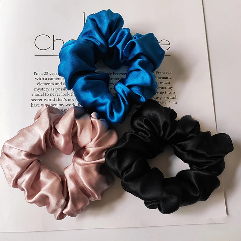 Tres gomas para el pelo de seda en azul, rosa y negro, con pliegues sobre fondo blanco.