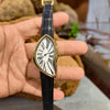 A hand holds a black leather fashion quartz wristwatch with a gold-toned Roman dial and hands.