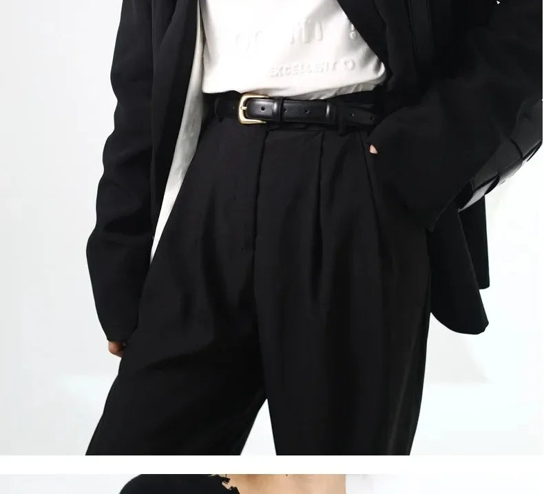 A close-up of a black belt worn over black trousers and a white shirt.