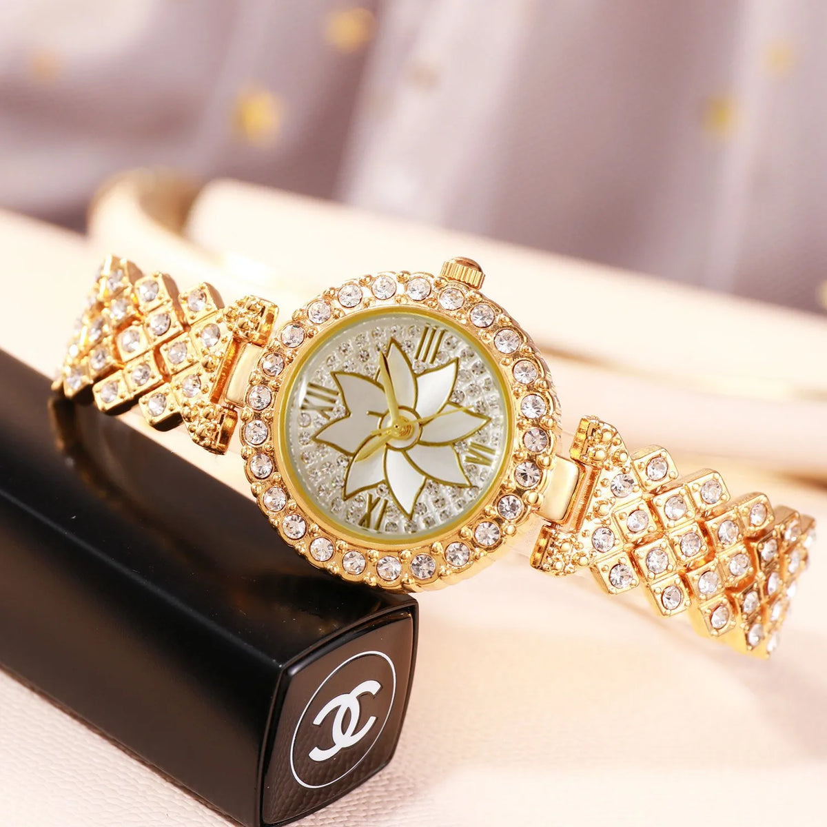 A gold-toned rhinestone quartz watch and bracelet set displayed on a black box.