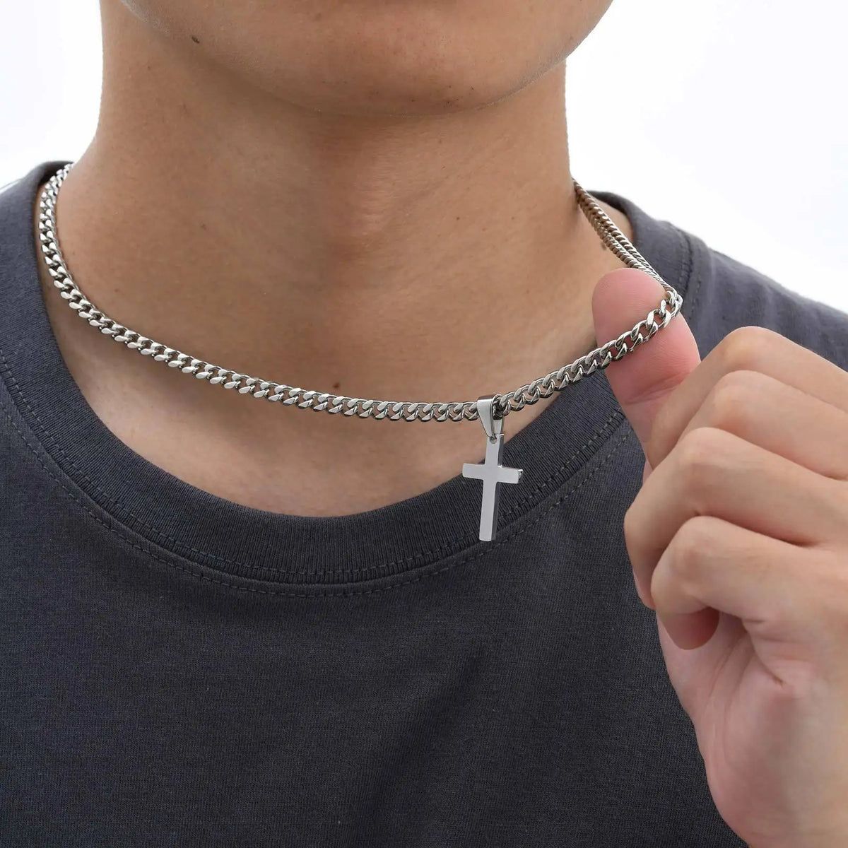 A close-up of a silver stainless steel Cuban link necklace with a cross pendant worn around a person's neck.