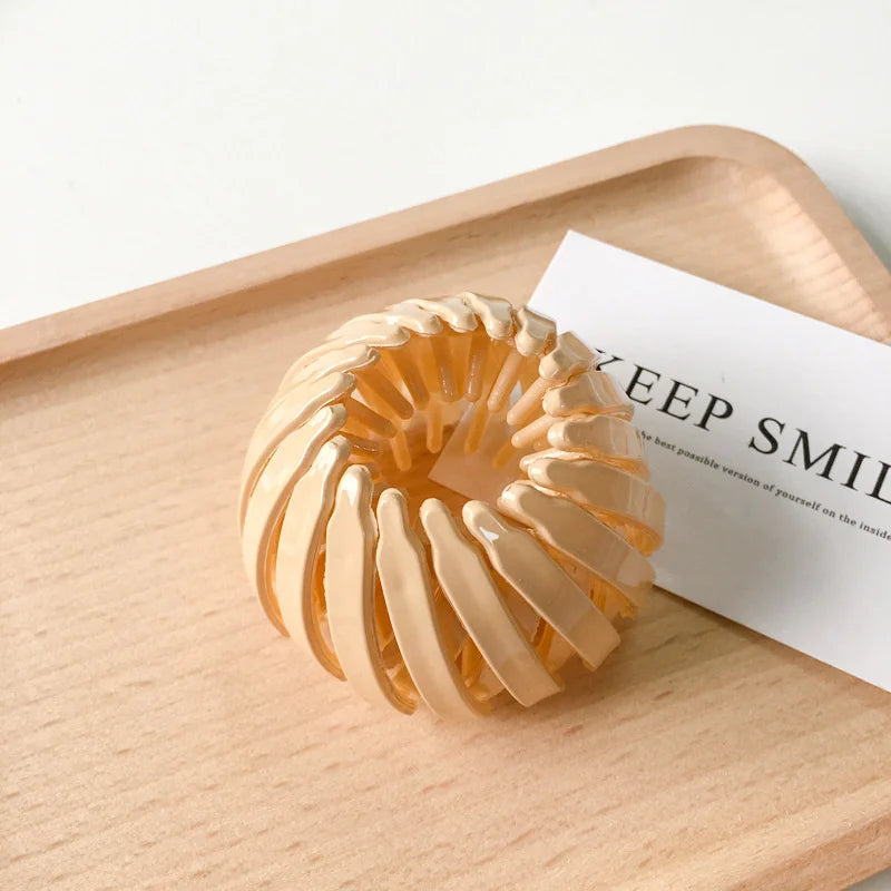 A close-up of elegant gold horsetail hair clips arranged in a circular pattern on a wooden tray.