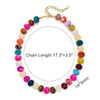 A colorful resin beaded statement choker necklace featuring various pink, purple, and amber beads on a gold chain.