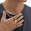 A close-up of a gold-colored stainless steel Cuban link necklace with a cross pendant worn around a neck.