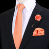 Chaqueta negra sobre camisa blanca y corbata de seda naranja con una flor rosa en la solapa.