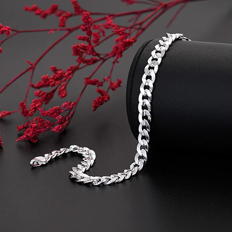 Un ensemble de collier et bracelet en argent affiché sur un fond noir avec du feuillage rouge.