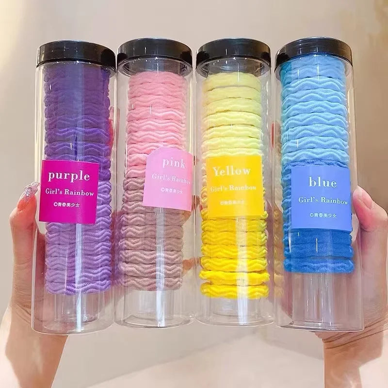 Cuatro recipientes de vidrio llenos de gomas para el cabello con rayas onduladas moradas, rosas, amarillas y azules.