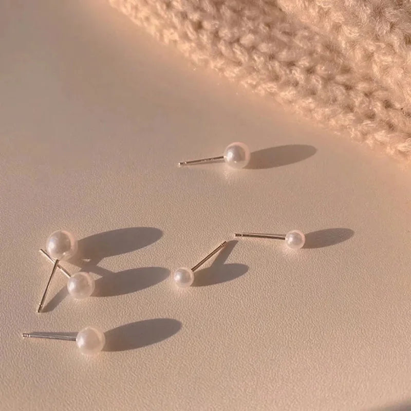 Three gold-toned stud earrings with round pearls are displayed on a light surface.