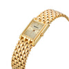 Gros plan d'une montre en quartz dorée avec un bracelet en maillons d'or jaune et un cadran rectangulaire.