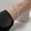 A close-up of a sterling silver double heart charm bracelet worn on a wrist against a light background.