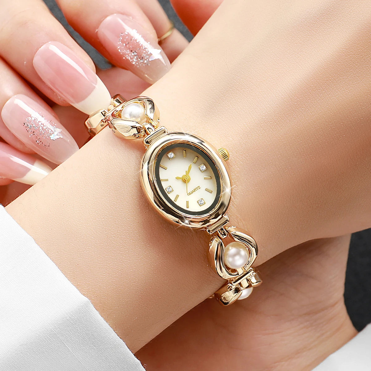 Nahaufnahme einer eleganten Gold- und Perlen-Quarz-Armbanduhr an einem Handgelenk mit gepflegten Nägeln.